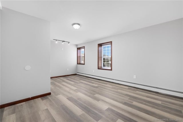 empty room featuring baseboards, a baseboard heating unit, and wood finished floors