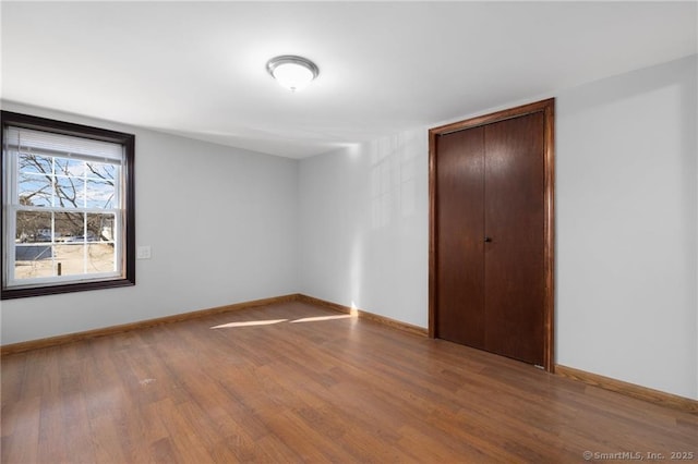 unfurnished bedroom with baseboards, wood finished floors, and a closet