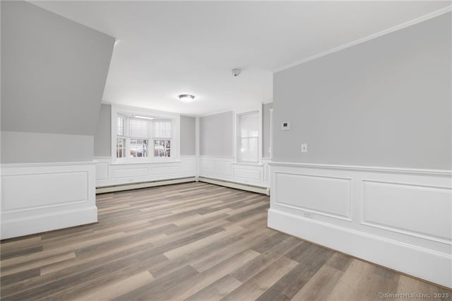 spare room featuring a baseboard radiator, wainscoting, crown molding, and wood finished floors