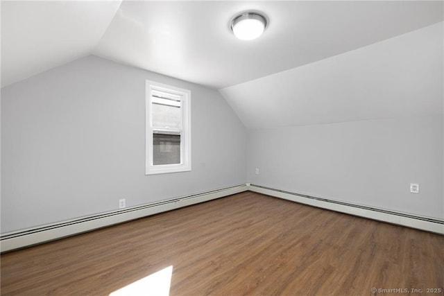 additional living space with wood finished floors, vaulted ceiling, a baseboard heating unit, and baseboard heating