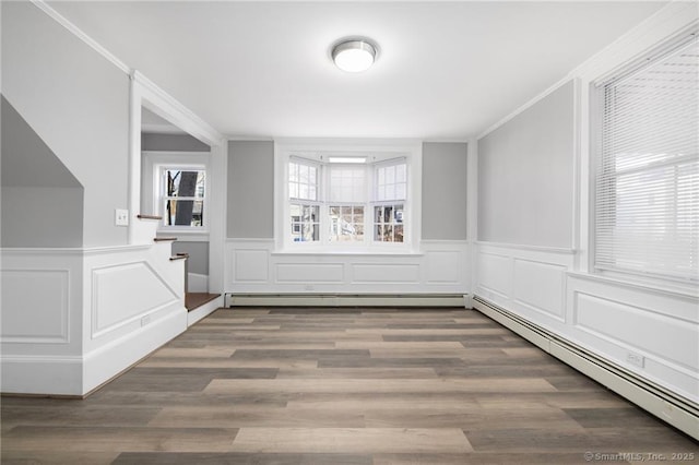 unfurnished room featuring baseboard heating, stairway, wood finished floors, and ornamental molding
