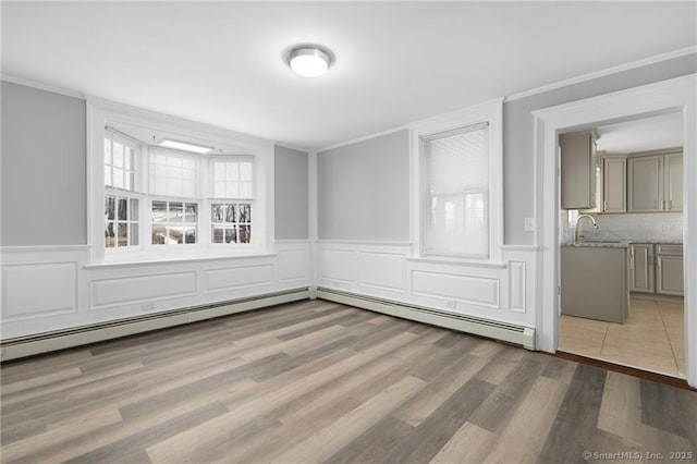 empty room featuring a baseboard radiator, a sink, crown molding, and wood finished floors