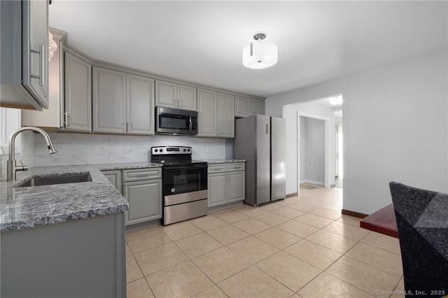 kitchen with stainless steel appliances, a sink, gray cabinetry, backsplash, and light tile patterned floors
