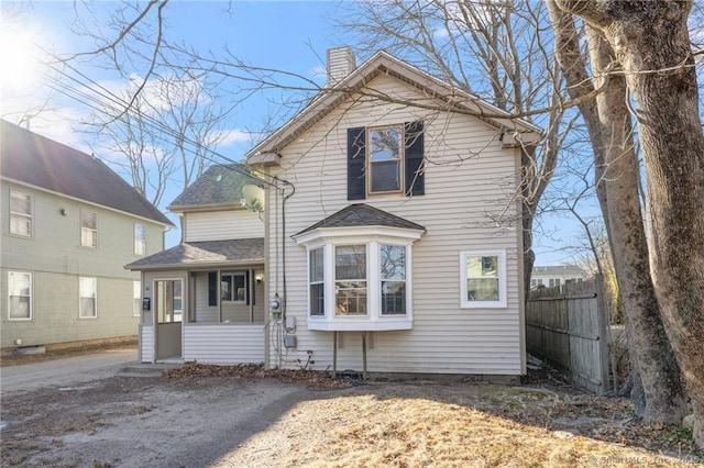 traditional-style home with a shingled roof, fence, and a chimney