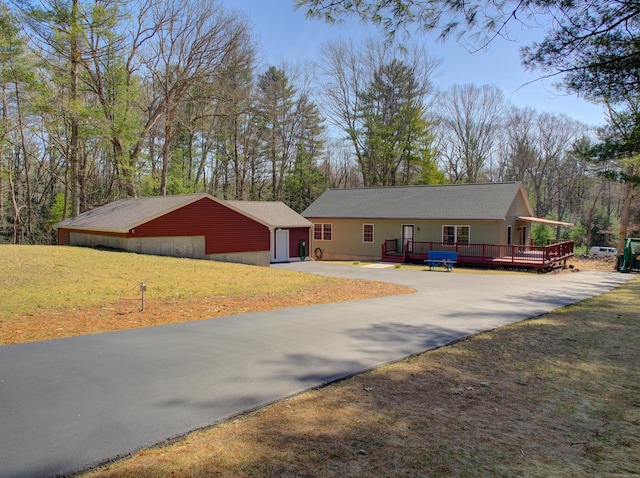 ranch-style house featuring driveway, a wooden deck, a detached garage, an outdoor structure, and a front lawn