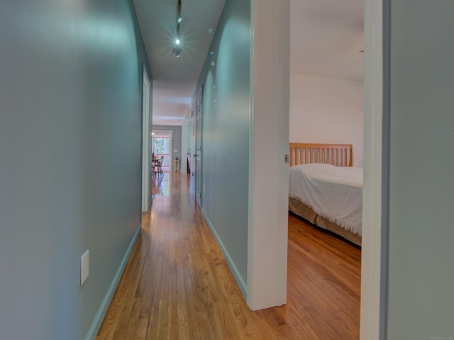 hall featuring track lighting, baseboards, and light wood finished floors