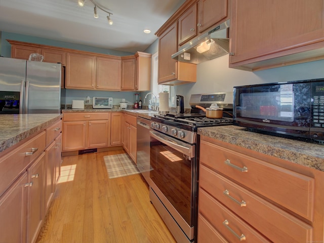 kitchen featuring appliances with stainless steel finishes, light stone counters, a sink, light wood finished floors, and under cabinet range hood