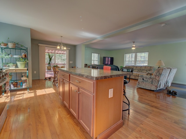 kitchen featuring a kitchen breakfast bar, a kitchen island, ceiling fan with notable chandelier, open floor plan, and light wood-style flooring
