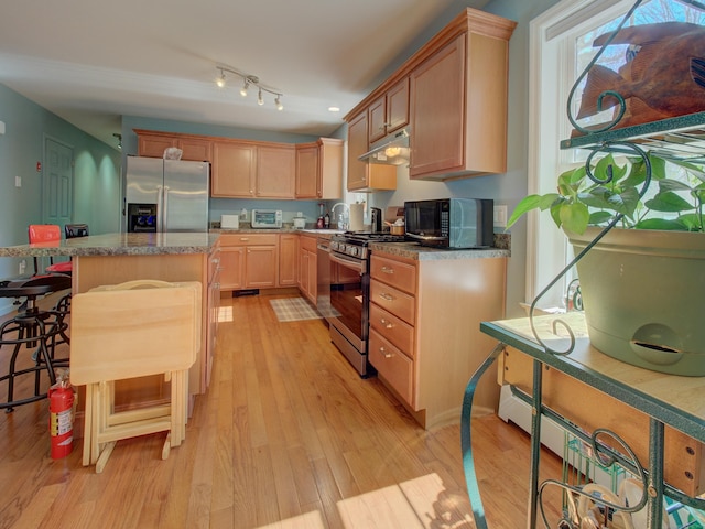 kitchen with light brown cabinetry, appliances with stainless steel finishes, a center island, light wood-type flooring, and under cabinet range hood