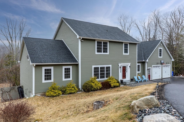 colonial home featuring roof with shingles, fence, a garage, and aphalt driveway
