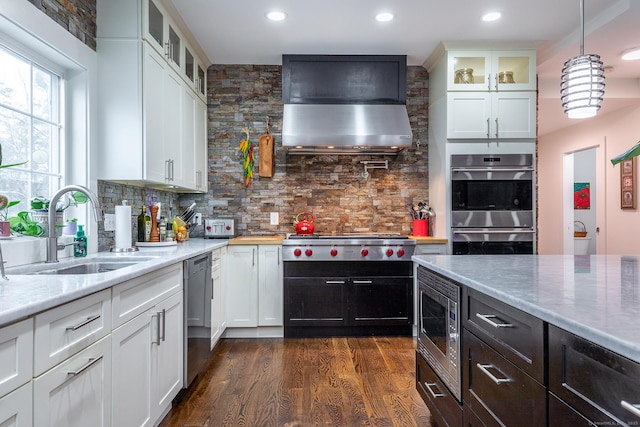 kitchen with wall chimney exhaust hood, dark wood finished floors, appliances with stainless steel finishes, white cabinetry, and a sink