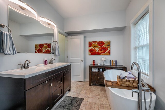 full bath featuring baseboards, double vanity, a sink, and a freestanding bath