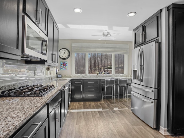 kitchen featuring light stone countertops, ceiling fan, stainless steel appliances, a sink, and backsplash