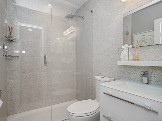 bathroom with tile walls, vanity, toilet, and a shower stall