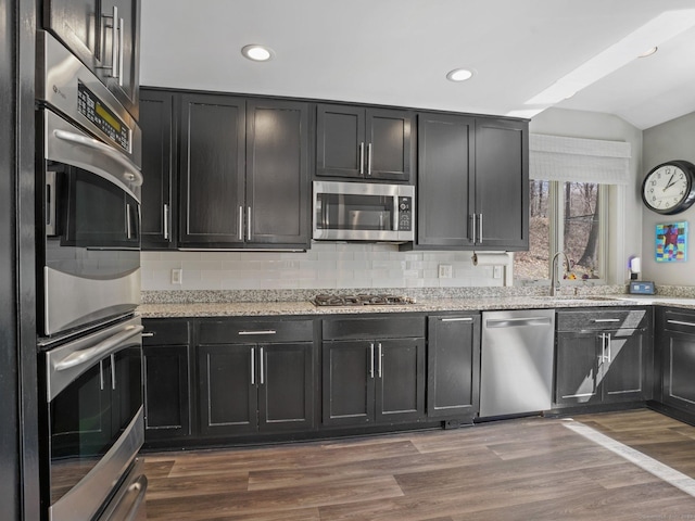 kitchen featuring backsplash, a sink, dark cabinetry, dark wood-style floors, and stainless steel appliances