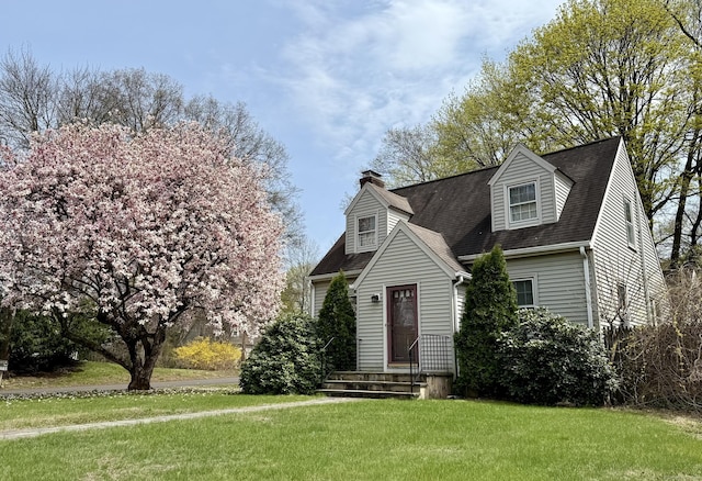 cape cod home with a shingled roof, a front lawn, and a chimney