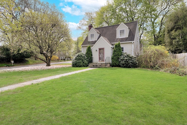 cape cod house with a chimney, fence, a front yard, and roof with shingles