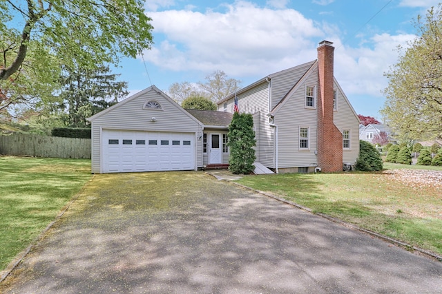 view of front facade featuring aphalt driveway, a chimney, fence, a front lawn, and a garage