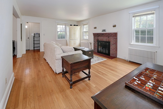 living room featuring a brick fireplace, baseboards, radiator heating unit, and light wood-style floors
