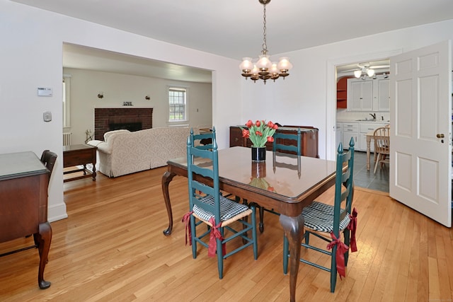 dining space with an inviting chandelier, light wood-style flooring, and a brick fireplace