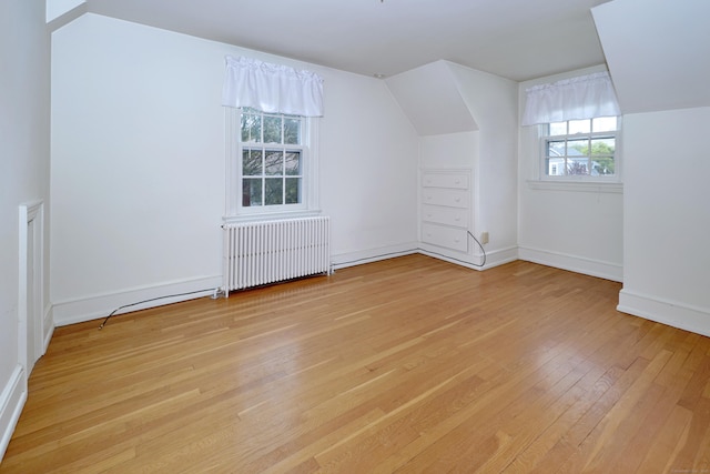 additional living space featuring baseboards, radiator heating unit, light wood-type flooring, and lofted ceiling