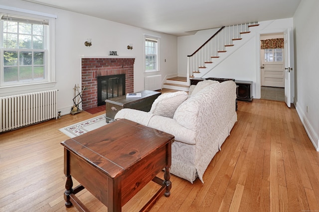 living area featuring radiator heating unit, a wealth of natural light, stairway, and light wood-type flooring