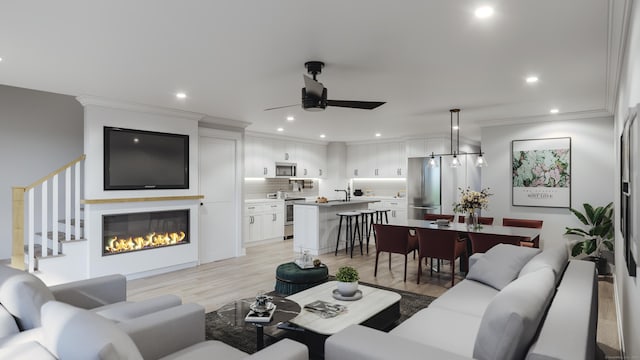 living area with ceiling fan, a glass covered fireplace, recessed lighting, light wood-type flooring, and ornamental molding