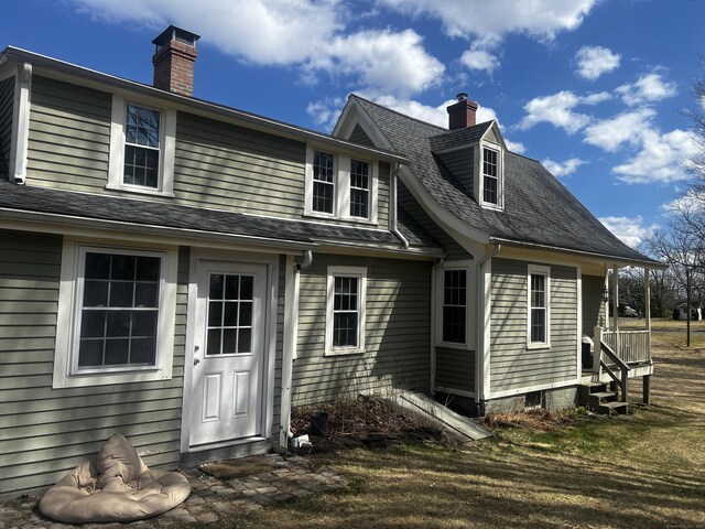 back of house with roof with shingles and a chimney