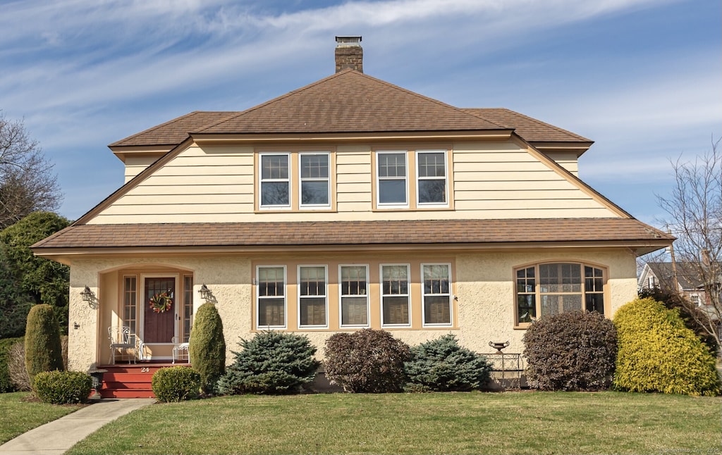 24 Woodland St, Wethersfield, CT 06109 - view of front of house with stucco siding, a chimney, a front yard, and roof with shingles