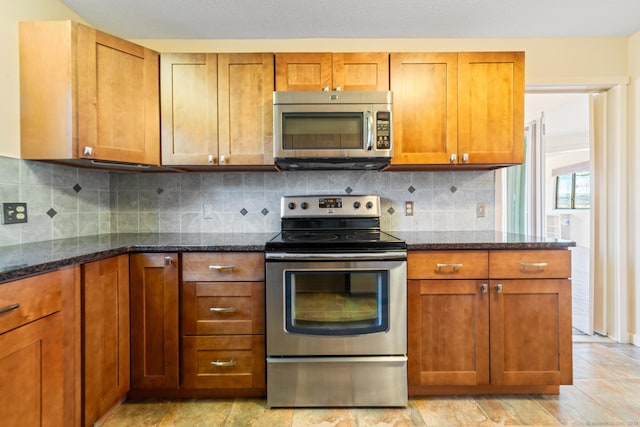 kitchen featuring dark stone counters, appliances with stainless steel finishes, brown cabinetry, and decorative backsplash