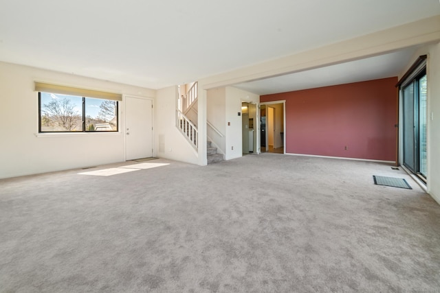 carpeted spare room with stairway and a healthy amount of sunlight