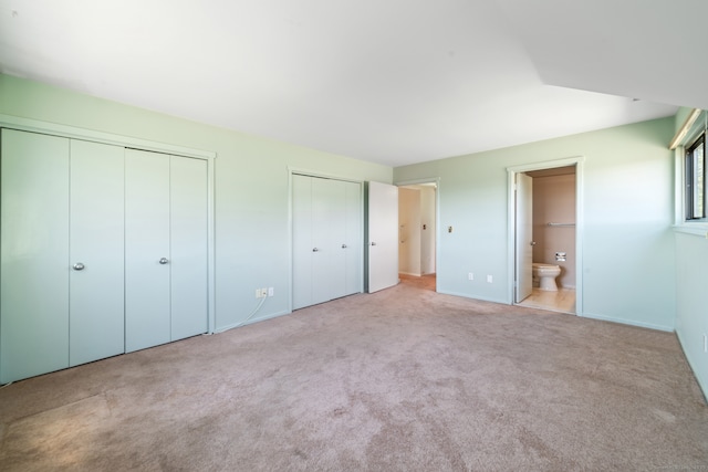 unfurnished bedroom with ensuite bath, carpet, and two closets