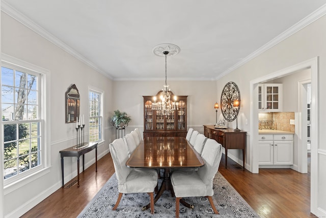 dining space featuring dark wood-type flooring, a notable chandelier, ornamental molding, and baseboards
