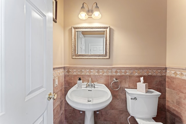 bathroom featuring wainscoting, tile walls, a sink, and toilet
