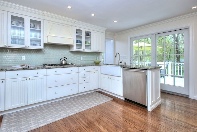 kitchen with stone countertops, a peninsula, wood finished floors, custom range hood, and appliances with stainless steel finishes