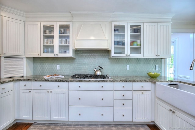 kitchen featuring ornamental molding, custom exhaust hood, dark stone counters, and tasteful backsplash