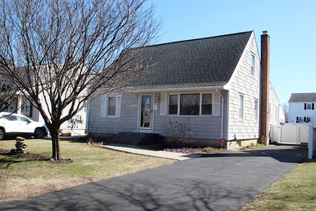 cape cod home with a chimney, a shingled roof, a front lawn, and a gate