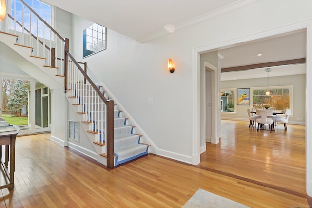 stairway with baseboards, a wealth of natural light, ornamental molding, and wood-type flooring