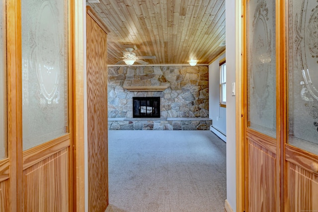 unfurnished living room featuring wood ceiling, ceiling fan, baseboard heating, carpet floors, and a stone fireplace
