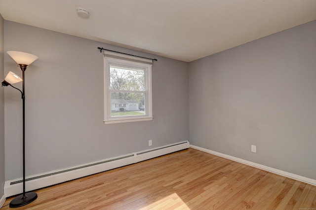 unfurnished room with a baseboard heating unit, wood finished floors, and baseboards