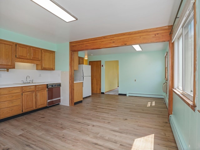 kitchen with a baseboard radiator, a sink, dishwashing machine, and freestanding refrigerator