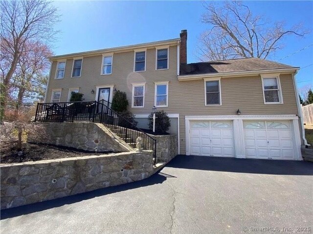 colonial-style house with a chimney, aphalt driveway, and an attached garage