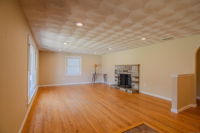 unfurnished living room with a stone fireplace, light wood finished floors, baseboards, and visible vents