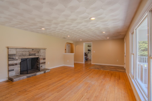 unfurnished living room featuring baseboards, light wood finished floors, a stone fireplace, and arched walkways