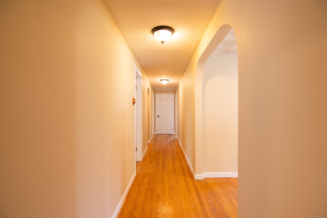 corridor with light wood-style floors, arched walkways, and baseboards