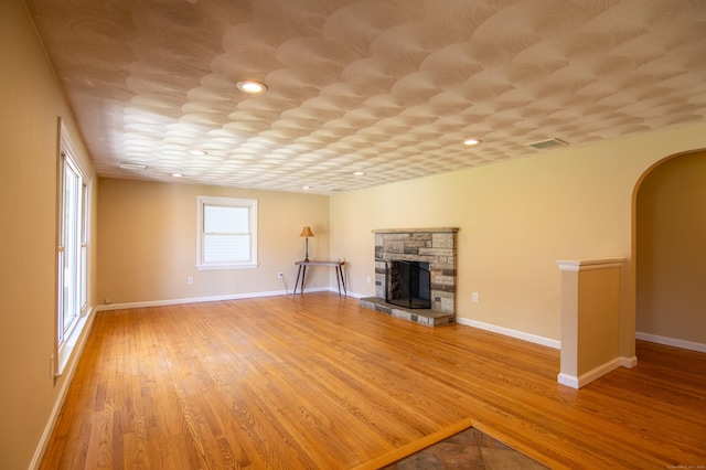 unfurnished living room featuring arched walkways, a stone fireplace, baseboards, wood finished floors, and visible vents