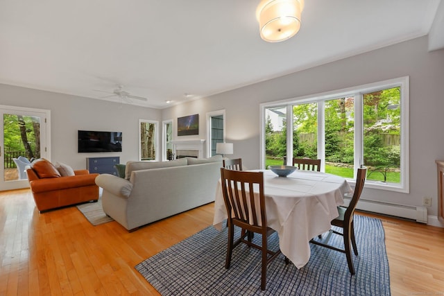 dining area featuring baseboard heating, light wood finished floors, a ceiling fan, a fireplace, and baseboards