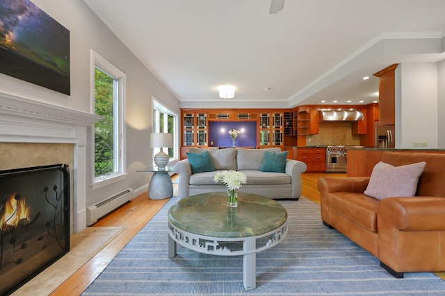 living room with baseboard heating, light wood-style floors, a high end fireplace, and ornamental molding