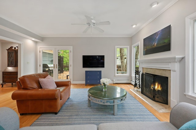 living room with a fireplace, a ceiling fan, wood finished floors, a baseboard radiator, and crown molding
