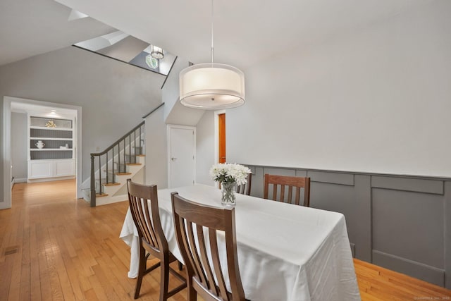 dining space with light wood-style floors, stairs, built in shelves, and vaulted ceiling